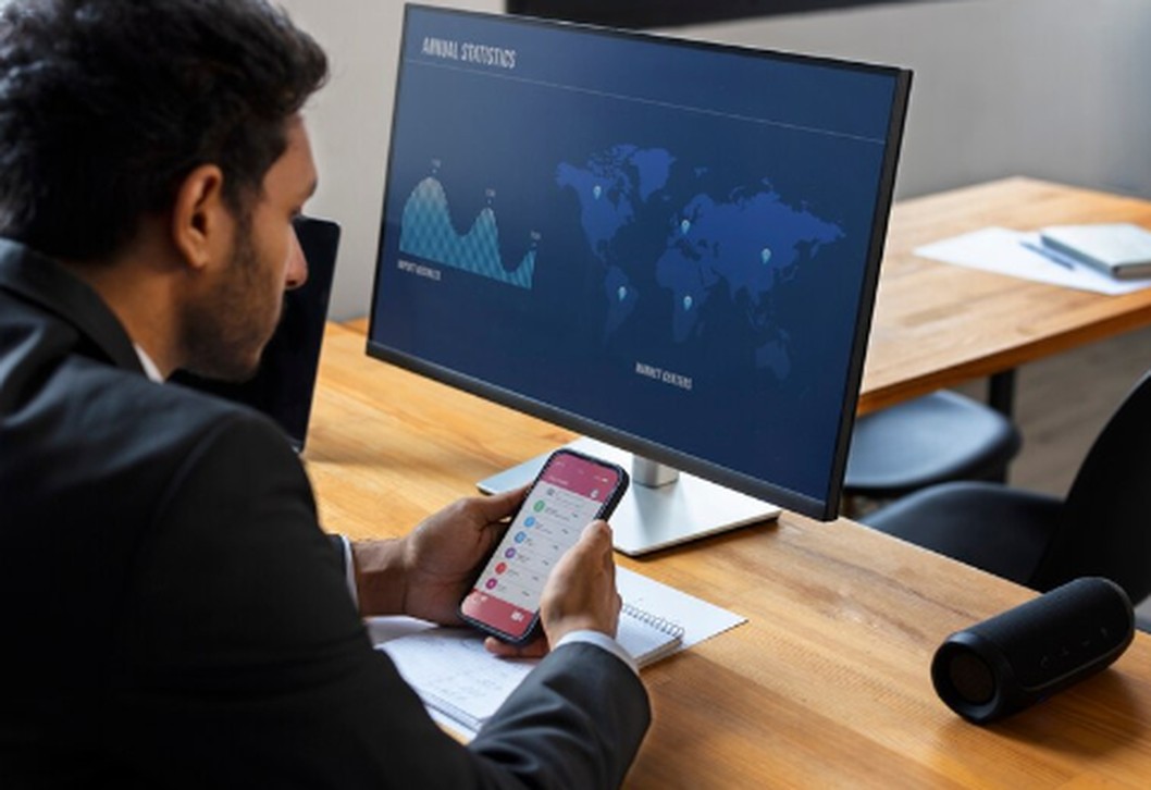 A businessman analyzing financial data on a smartphone while referencing a digital dashboard displaying global charts and statistics, representing the modern approach to monitoring Sectoral Investment Trends in real time.