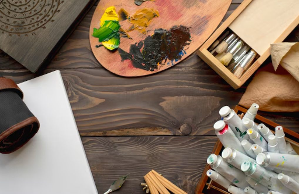 A wooden table with paint tubes, brushes, a colour palette, and drawing supplies, symbolising creativity and the value of art and collectibles funds in alternative investments.