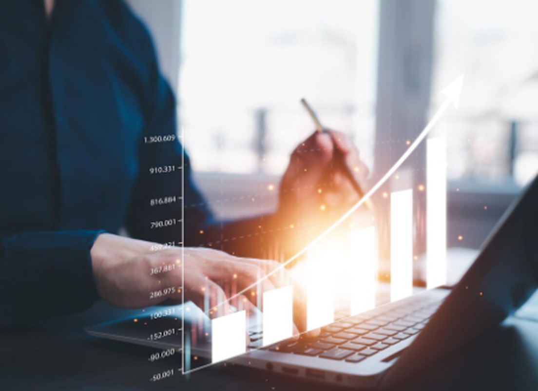 A person working on a laptop with a rising bar and line graph overlay, symbolising the growth potential of an investment asset in the financial market.