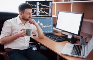A financial analyst monitoring stock market charts on multiple screens while holding a cup of coffee, reflecting the challenges and opportunities of investing in small caps.